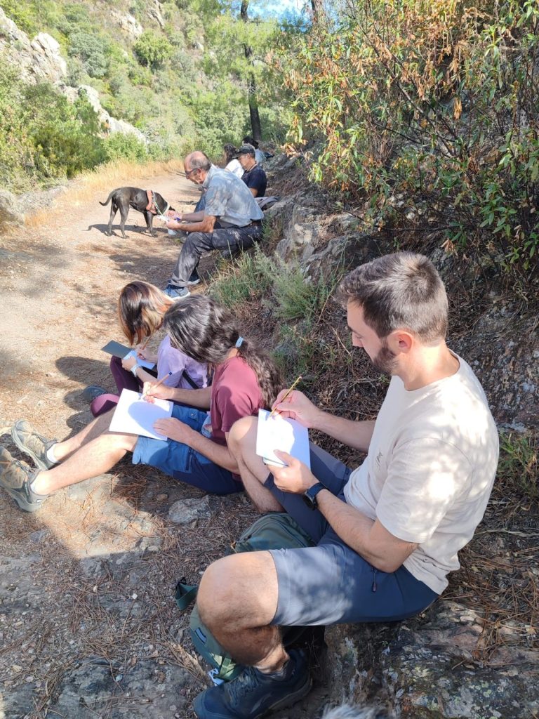 Participantes dibujando sentados al borde del camino en la Georruta de Los Molinos