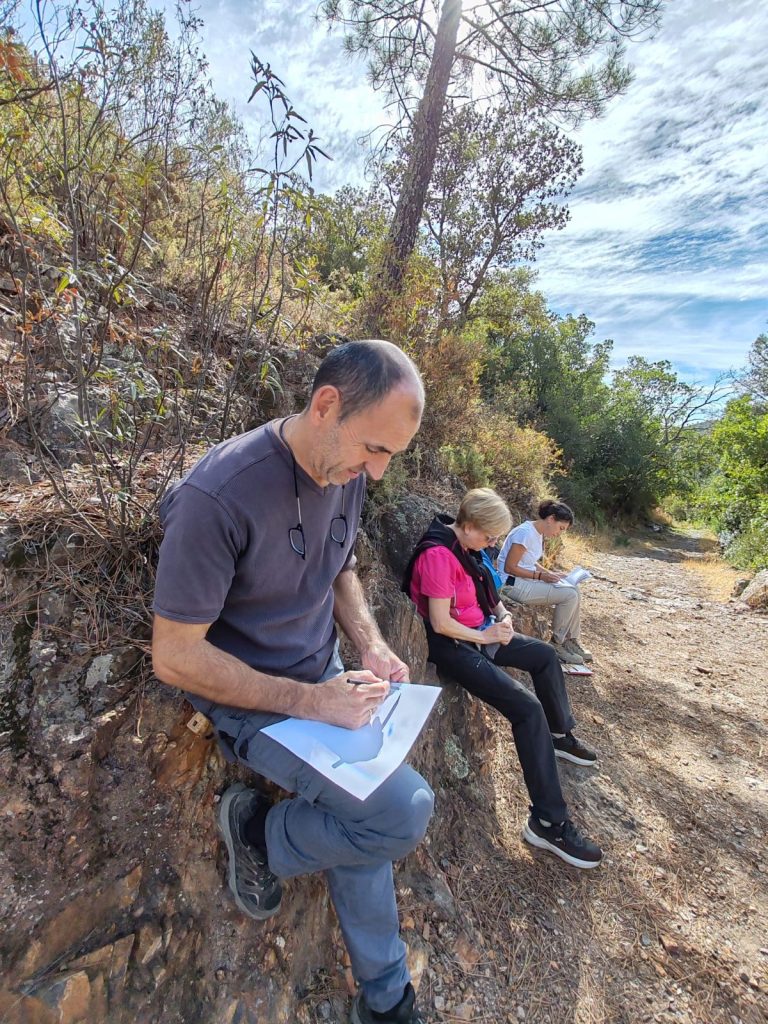 Participantes dibujando sentados sobre las rocas del camino en la Georruta de Los Molinos